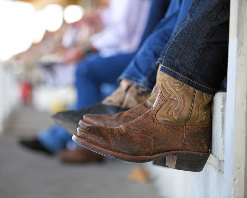 Closeup of dangling legs in bleachers wearing cowboy boots at rodeo event